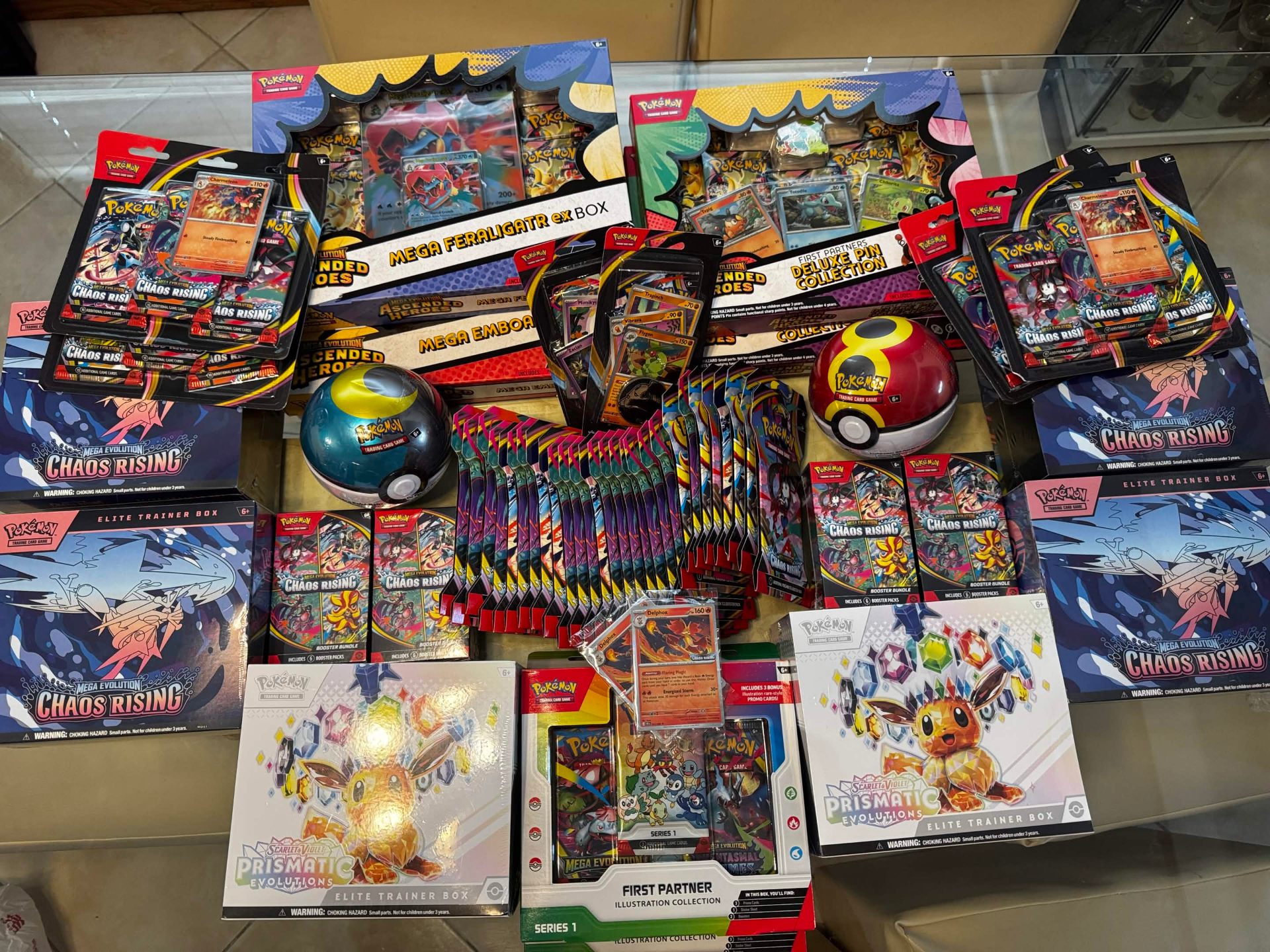 Massive table spread of Pokemon TCG products including Chaos Rising and Prismatic Evolutions